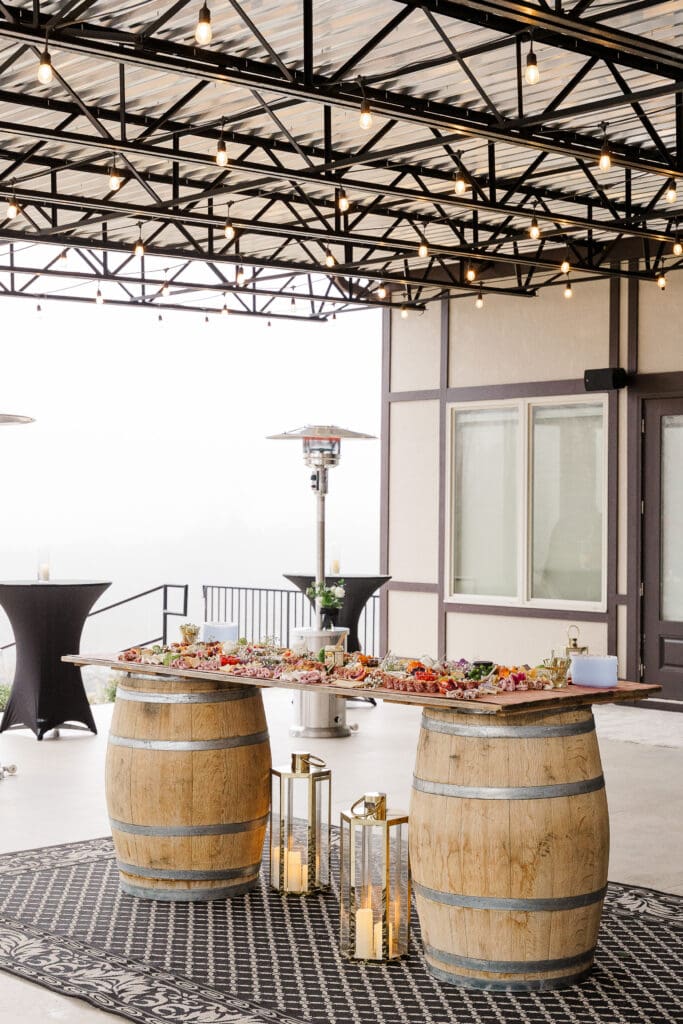 Cocktail hour setup with charcuterie table on wine barrels and gold lanterns at Venue In The Vines.