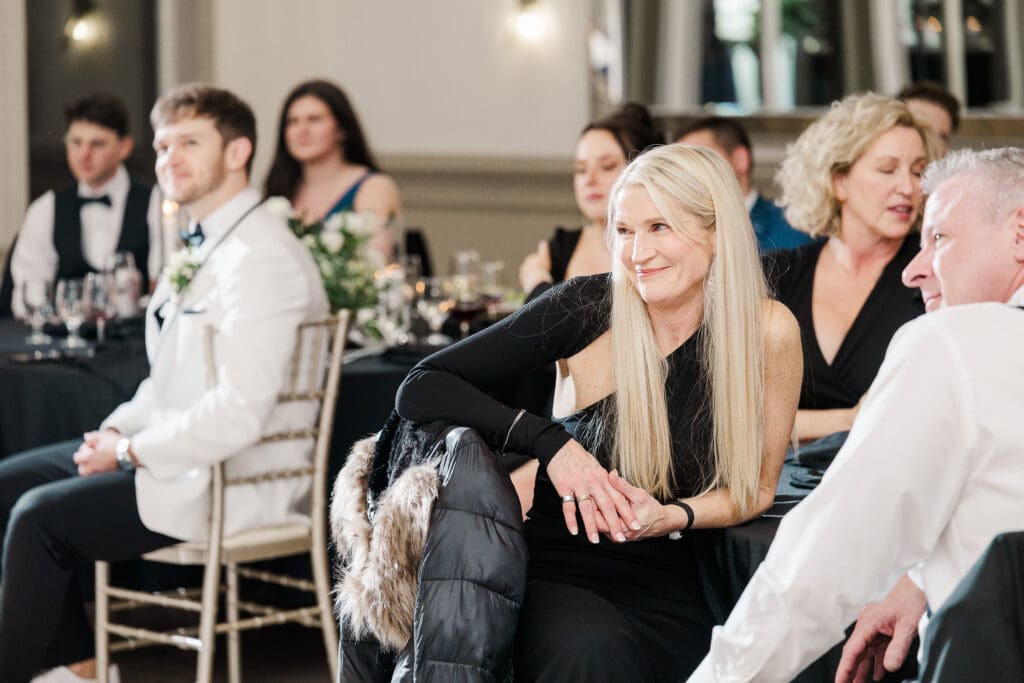Mother of the groom, guests, and the groom smiling with tearful emotion as the bride shares a first dance with her father.