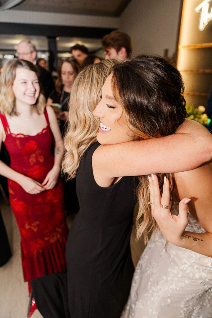 Bride hugs a guest with joyful laughter during evening wedding celebration.