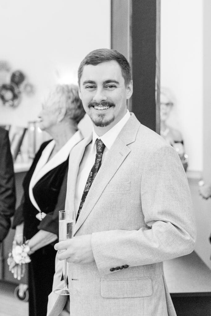 candid of guest holding champagne glass with warm smile during cocktail hour indoors.