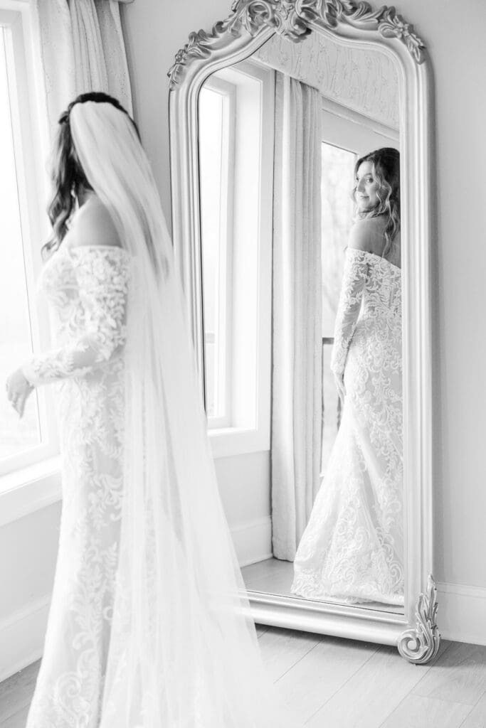 Bride reflected in ornate mirror wearing lace gown and long veil.