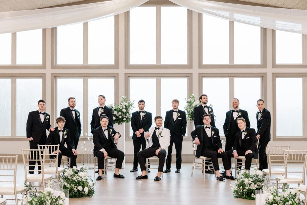 Groom and groomsmen pose in black tuxedos with white florals at Venue In The Vines in Ellijay, GA.