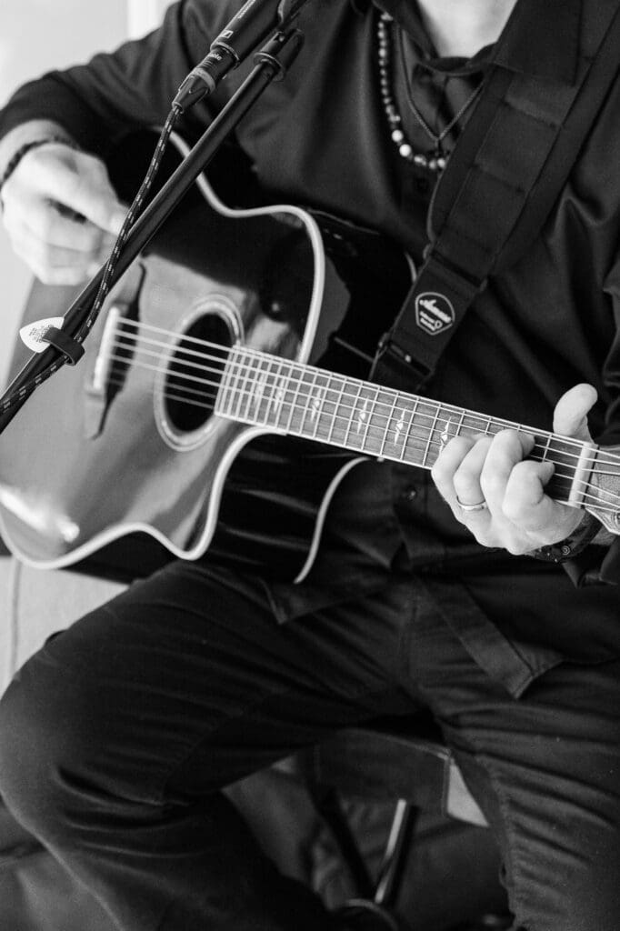 Close-up of musician Ace Suggs strumming a black acoustic guitar during wedding cocktail hour.