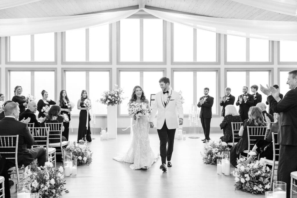 Bride and groom walk joyfully back down the aisle as guests cheer and applaud their just-married moment.