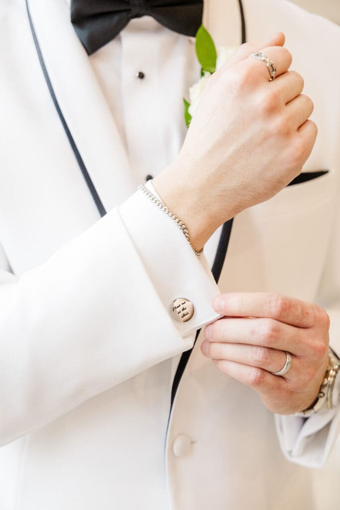 Close-up of groom adjusting his watch in a white tuxedo jacket with boutonniere detail.