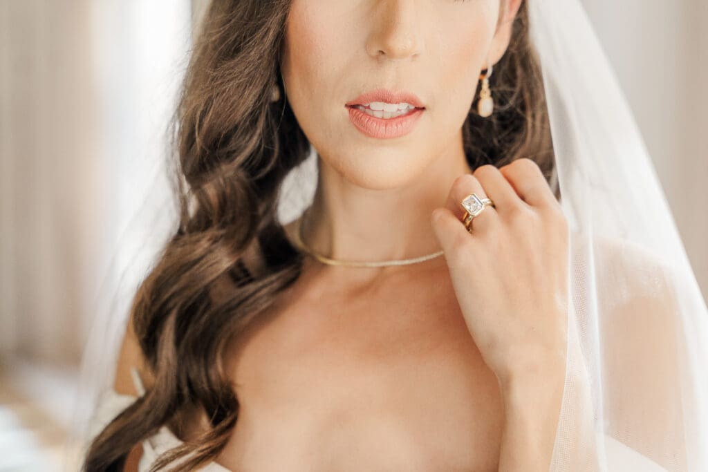 Close-up of an Atlanta GA bride on her wedding day, showcasing her diamond engagement ring, soft natural makeup, and flowing wavy hair under a delicate veil.