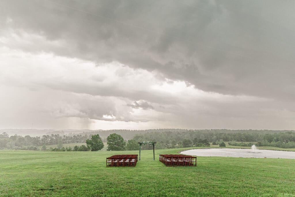 Outdoor wedding ceremony setup with wooden chairs and floral arbor under dramatic storm clouds at an Madison Georgia wedding venue.