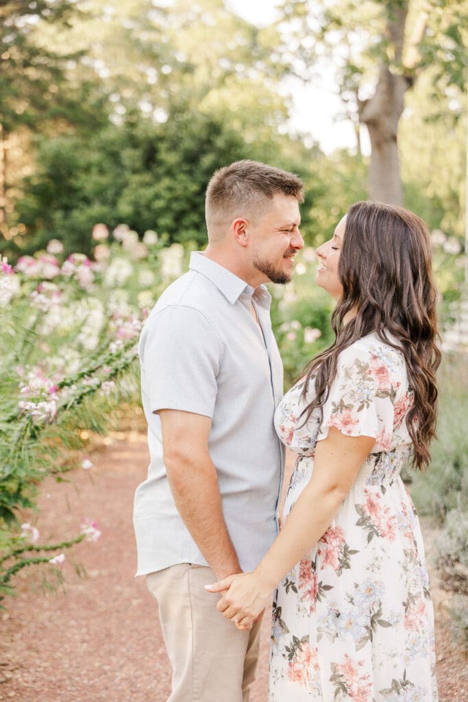 Engaged couple holding hands and smiling at each other in a blooming garden during their engagement session at Barrington Hall. Photo by Shanle Bowen, Atlanta GA Wedding & Engagement Photographer.